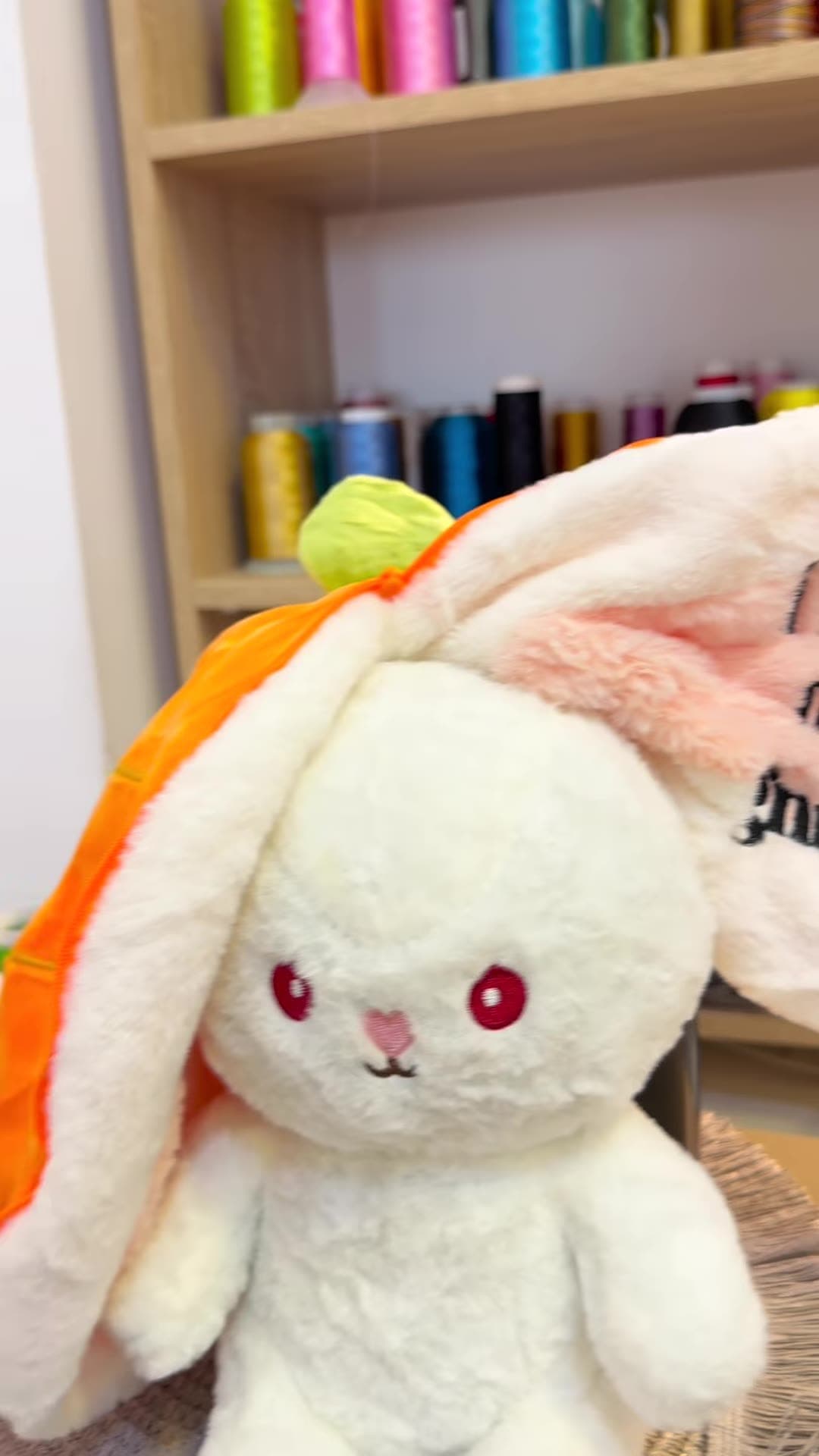Peluche lapin terminée, oreille brodée « i love my gnina », devant le mur de bobines